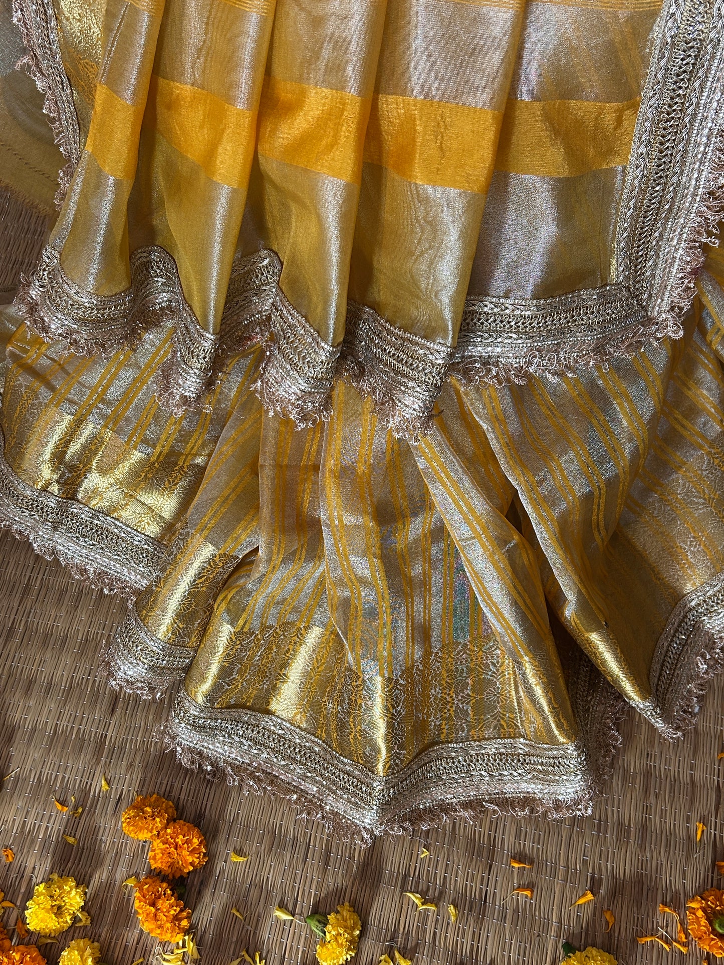 Close-up of a gold and silver saree with decorative elements on a wooden surface.